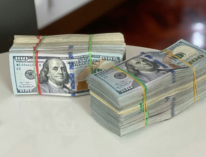 Stacks of hundred-dollar bills secured with rubber bands on a white table, highlighting cruelty linked to money and power.