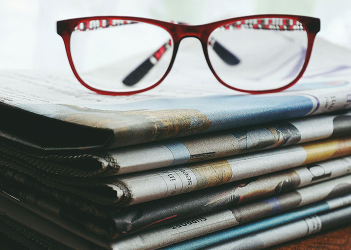 Red-framed glasses resting on a stack of newspapers, symbolizing people using loopholes against horrible bosses.