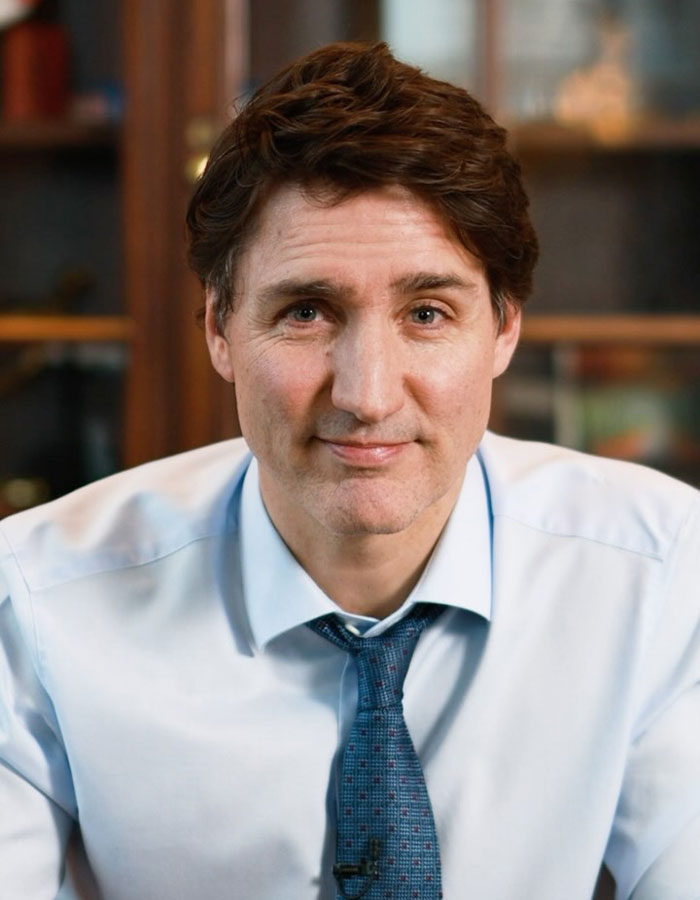 Justin Trudeau in a light blue shirt and tie, sitting indoors with a neutral expression, related to romance and midlife crisis.