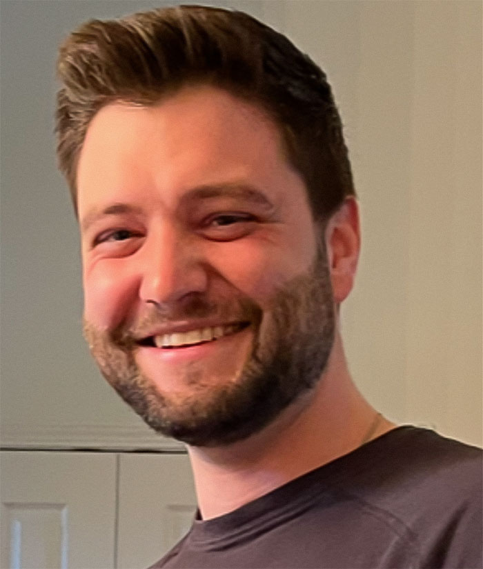 Smiling man with beard indoors, related to officials revealing cause of passing of couple found lifeless in car.