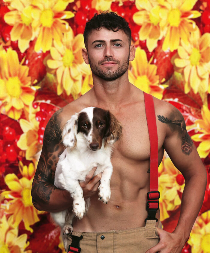 Shirtless firefighter holding an adorable dog against a bright floral background for Australian calendar photos.