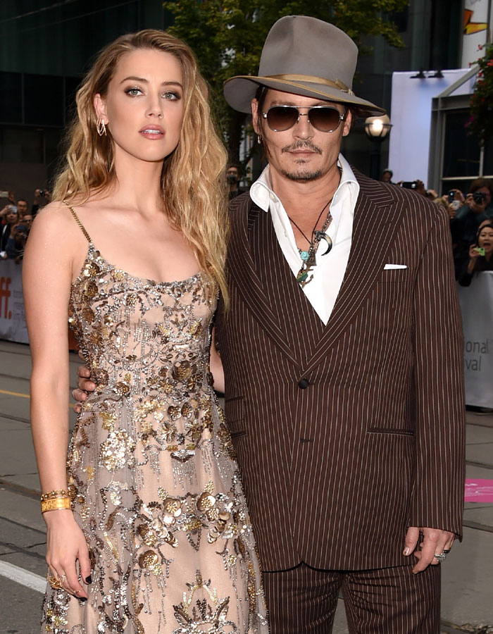 Johnny Depp wearing a hat and pinstripe suit with a woman in an embellished dress at a film event.