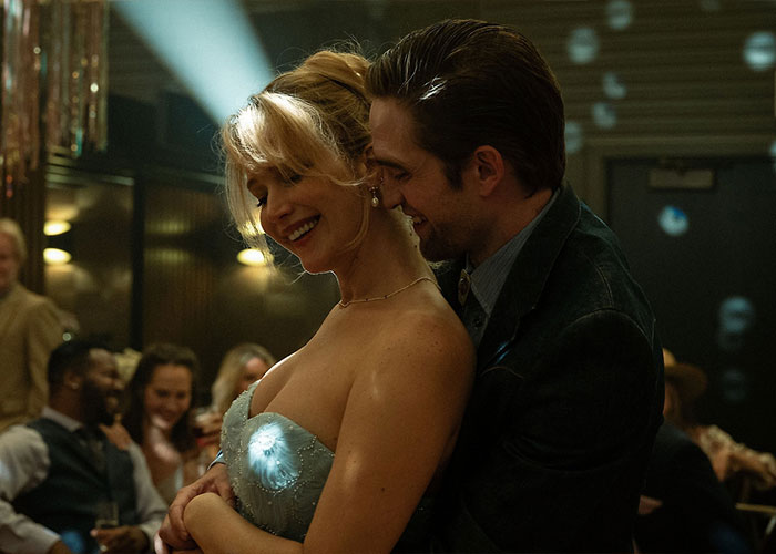 Jennifer Lawrence embraces a man in a dimly lit setting, highlighting discussions about plastic surgery plans and fan reactions.