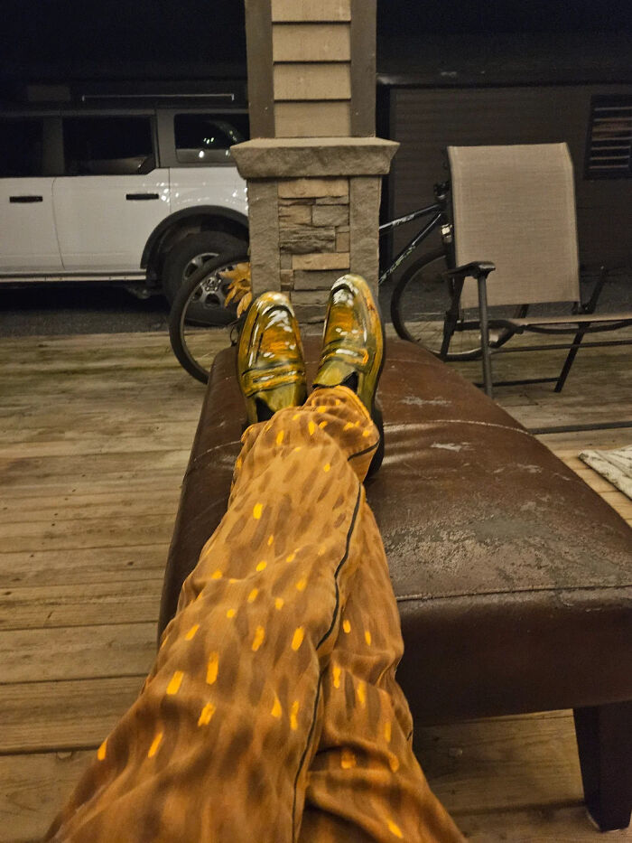 Artist wearing hand-painted Vincent van Gogh costume pants and shoes, relaxing on a brown lounge at night outdoors.