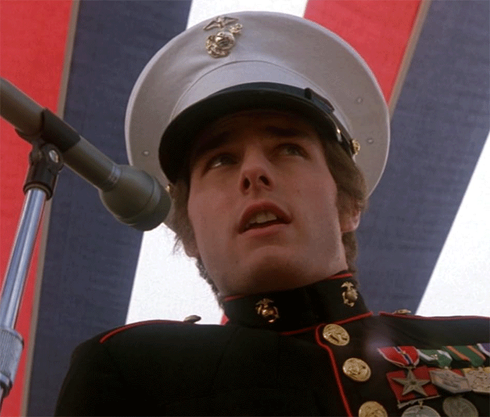 Tom Cruise in a military uniform speaking into a microphone during a public event or ceremony. Tom Cruise in a military uniform speaking into a microphone during a public event or ceremony.