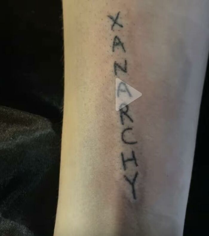 Tattoo of the word anarchy vertically inked on a forearm in a rough, hand-drawn style among unusual tattoos.