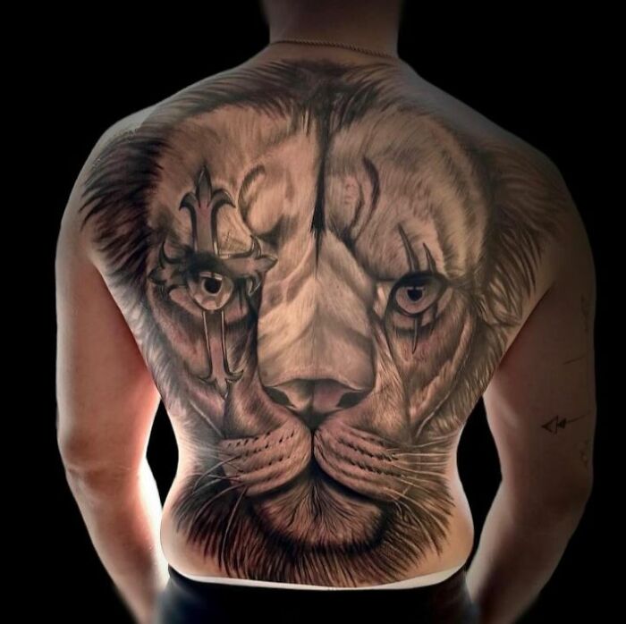 Realistic lion tattoo covering entire back with detailed shading and tribal elements in permanent body tattoo design.