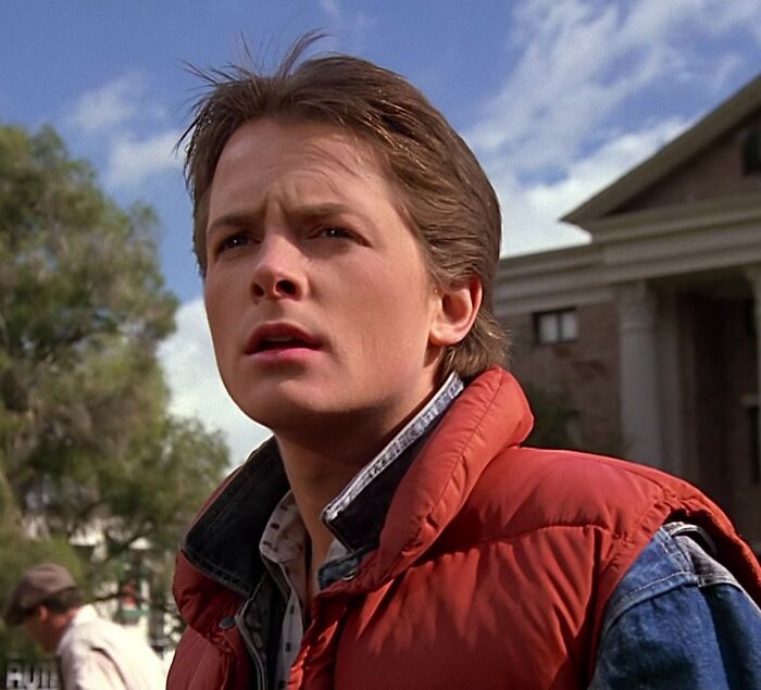 Michael J. Fox in an outdoor scene wearing a red puffer vest, related to a heartbreaking health update.