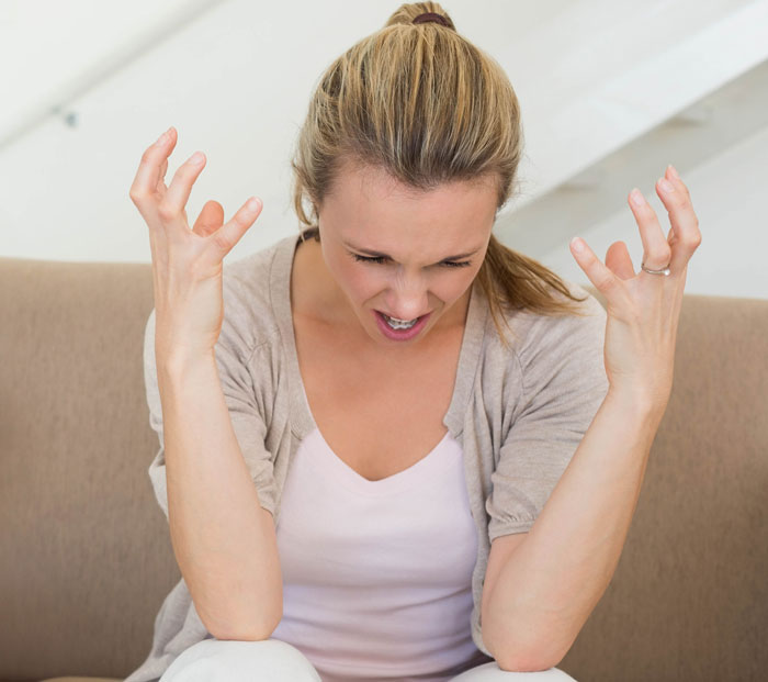Frustrated woman sitting on couch with hands raised, upset about on-site landlord actions and rent increase.