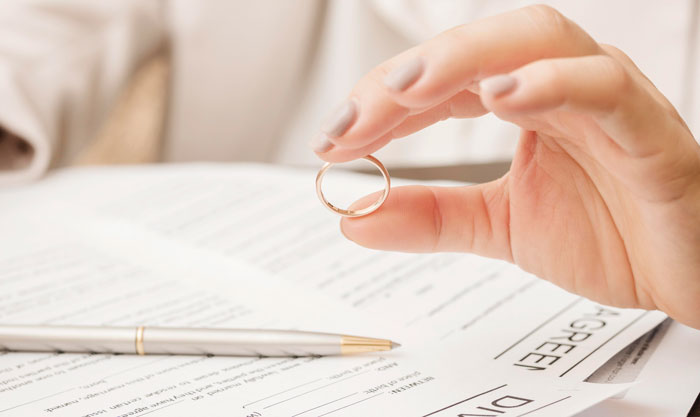 Hand holding a wedding ring over divorce papers, symbolizing a woman rethinking her marriage after a disturbing confession.