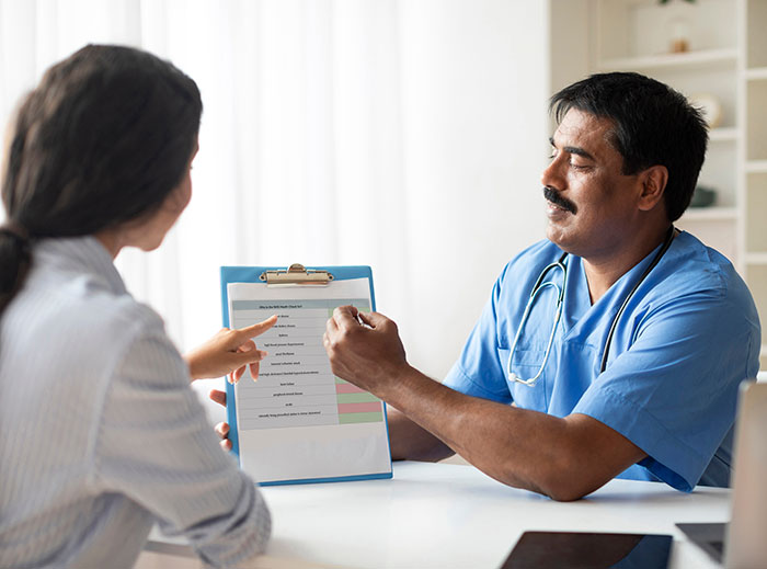 Doctor in blue scrubs explaining UK health guidance benefits of marrying your cousin to female patient in office.