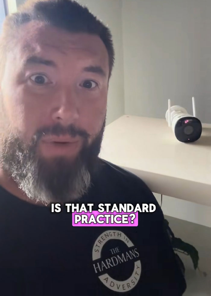 Man with beard and surprised expression beside a security camera in rental house after disturbing discovery by family rushing out