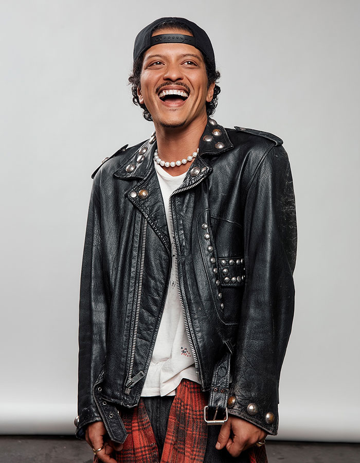 Man wearing a black leather jacket and backwards cap smiling, representing famous men who are much shorter than fans imagined