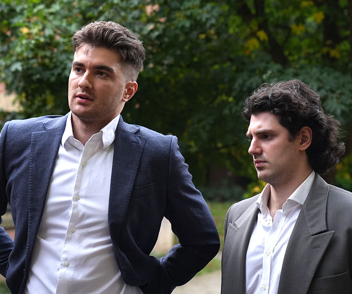 Two men in suits outdoors, appearing serious while discussing coroner findings on chemo refusal influence. Two men in suits outdoors, appearing serious while discussing coroner findings on chemo refusal influence.