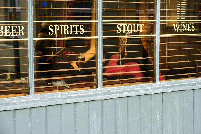 People inside a bar seen through window blinds with words beer, spirits, stout, and wines in street photography style capturing life moments.