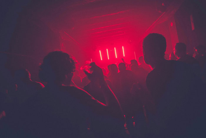 Crowd of people in a dark club with red lights, capturing the wildest we need to leave right now stories atmosphere.