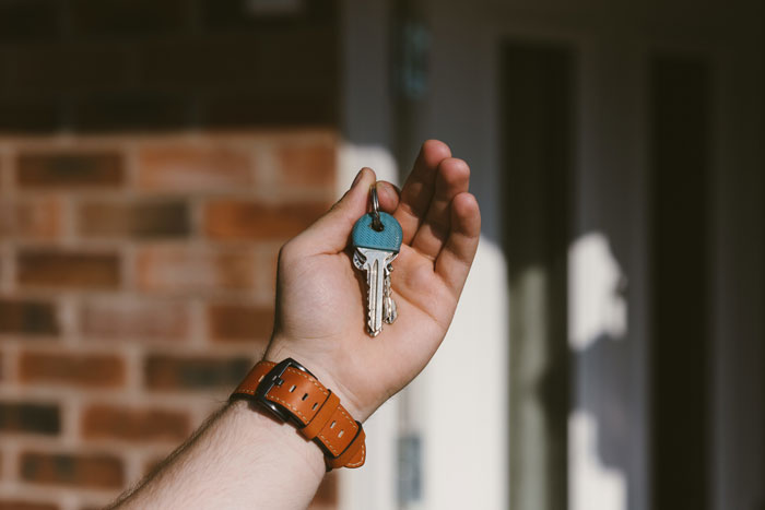 Hand holding house keys with a brick wall background, representing unexpected and awkward moments at work.