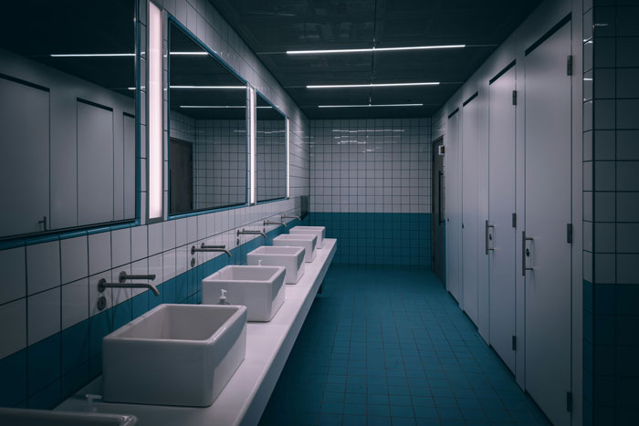 Public bathroom sinks and stalls with tiled walls highlighting toilet paper danger in public bathrooms warning.