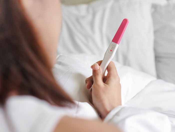 Person lying in bed holding a pregnancy test with a negative result, reflecting family secrets daycare workers heard