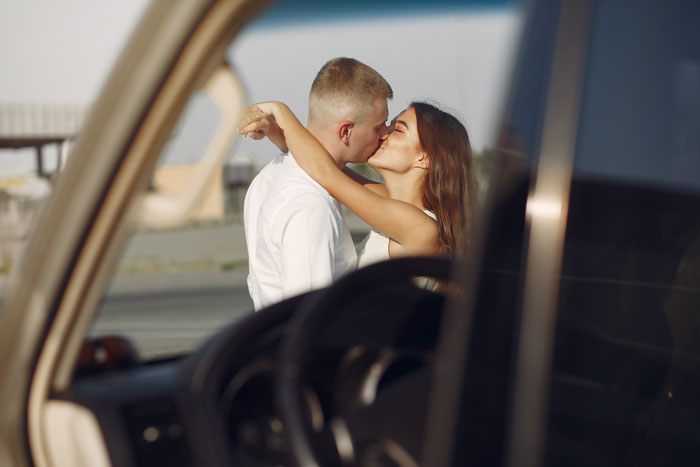 Couple kissing passionately outdoors, blurred car interior in foreground, contrasting with theme of cruel person revealed by people.