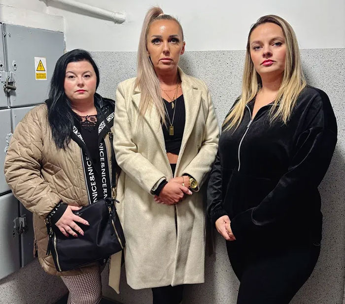 Three women standing indoors in coats and jackets, related to woman missing for 27 years found emaciated story.