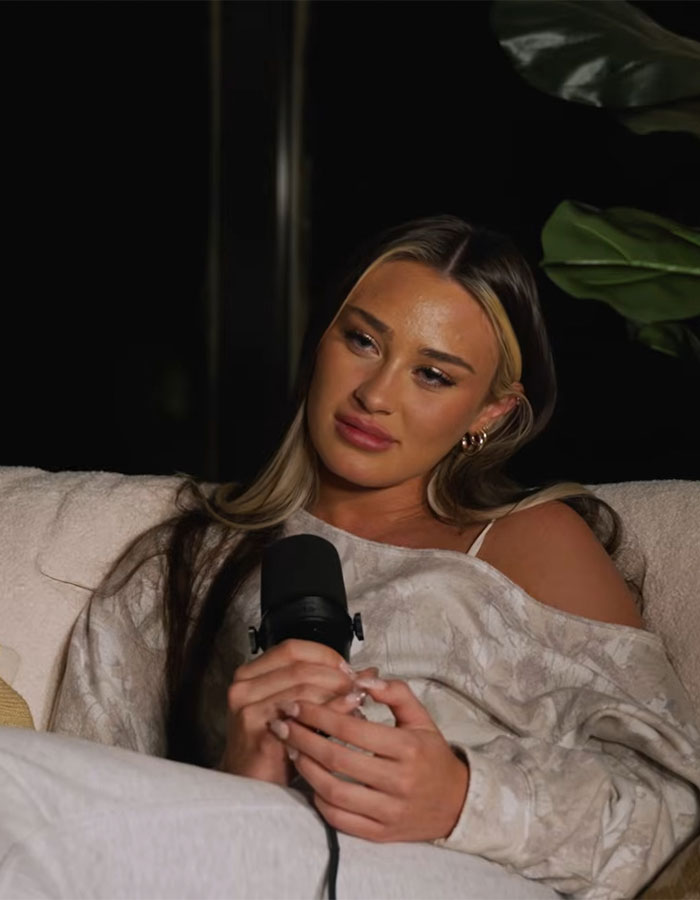 Adult star holding a microphone, sitting on a couch, reflecting on humiliating wedding vows and splitting from YouTube prankster.