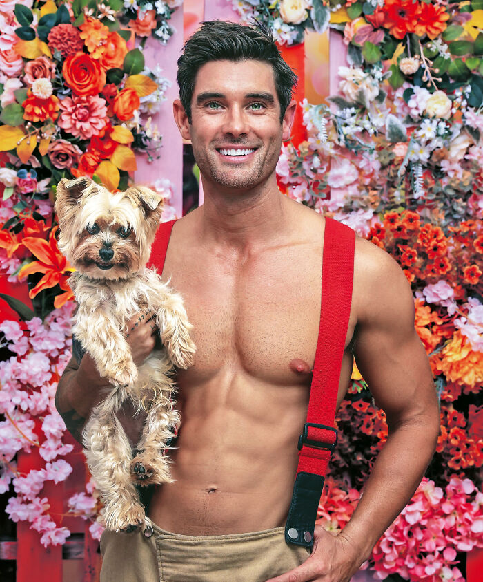 Shirtless firefighter with red suspenders holding a small dog against a vibrant floral background for Australian calendar.