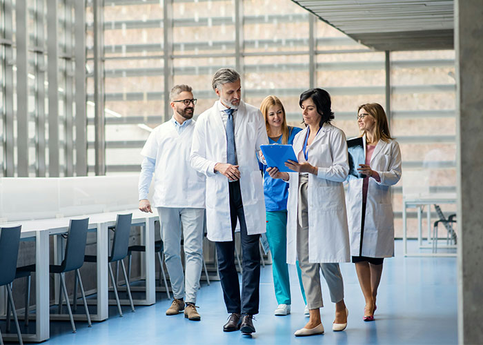 Group of scientists in lab coats discussing research findings while walking in a modern bright laboratory setting Group of scientists in lab coats discussing research findings while walking in a modern bright laboratory setting