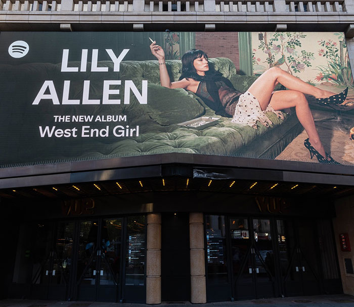 Billboard showing a woman reclining on a sofa with text referencing David Harbour's viral atrocious interaction involving a woman half his age.