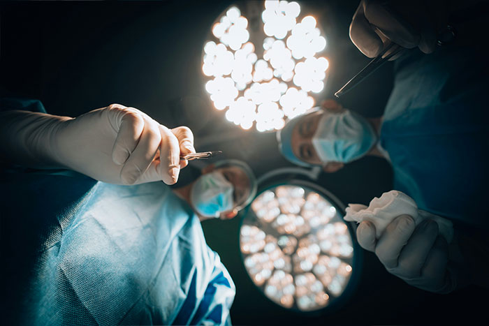 Surgeons in blue scrubs and masks performing a cosmetic surgery under bright operating room lights.
