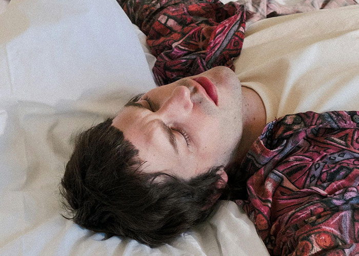 Young man lying down asleep on bed wearing a patterned shirt, evoking a creepy feeling related to things women said or did to men.