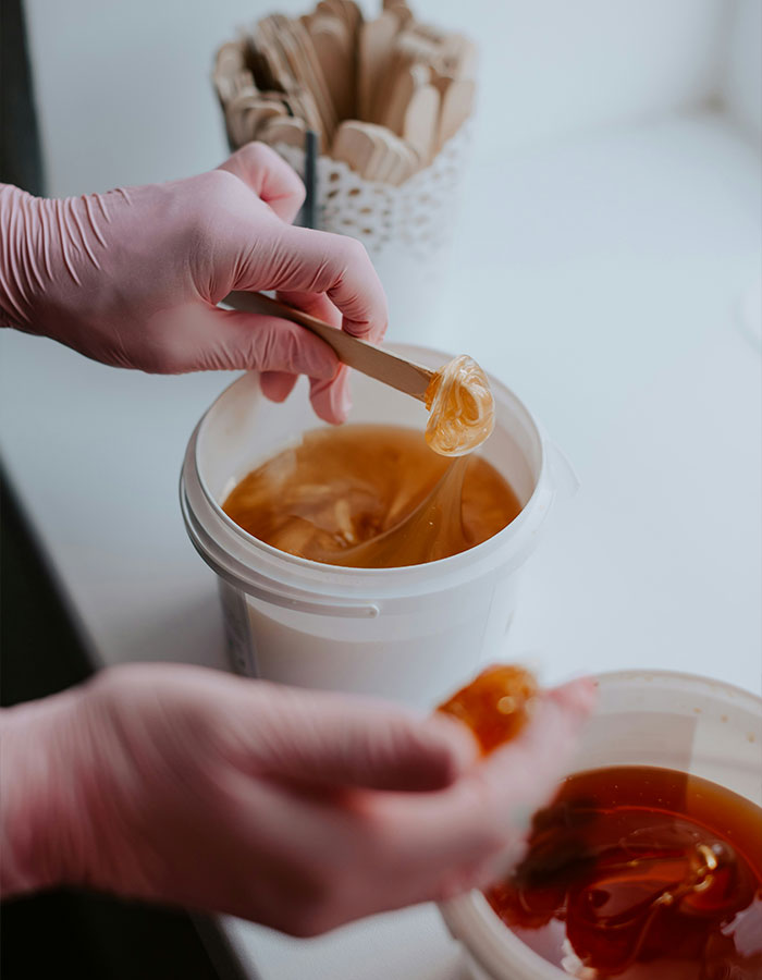 Aesthetician wearing pink gloves handling golden wax during beauty treatment in a clean, bright workspace.