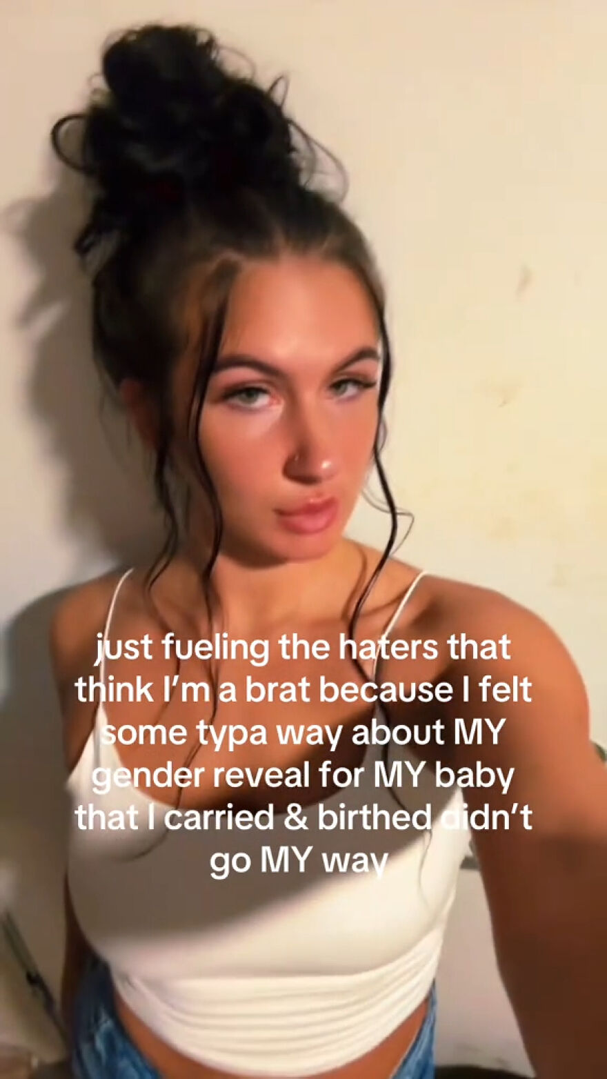 Woman with hair in a bun expressing frustration about her gender reveal and ex-mother-in-law in a casual indoor setting.