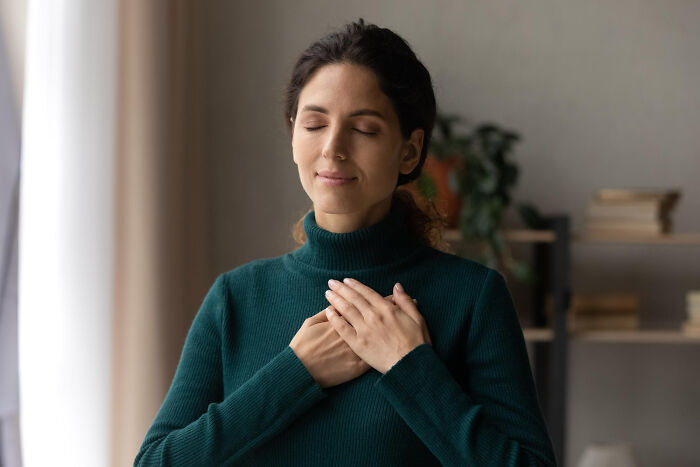 Woman in green sweater with eyes closed, hands on chest, symbolizing realization of life hacks tricking extra work.