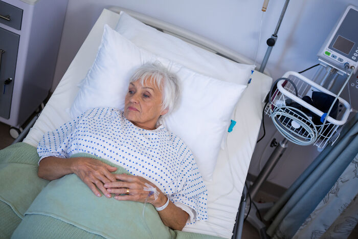 Elderly woman lying in hospital bed looking worried, setting for scary ghost stories hospital work theme.