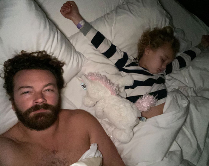 Danny Masterson lying in bed shirtless next to a sleeping child with a stuffed unicorn, highlighting Bijou Phillips relationship news.