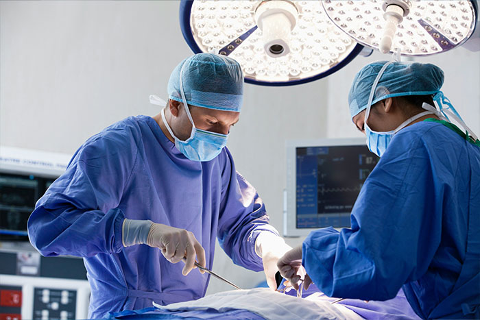 Two surgeons in an operating room performing urgent surgery related to a man with a 4-lb face tumor.