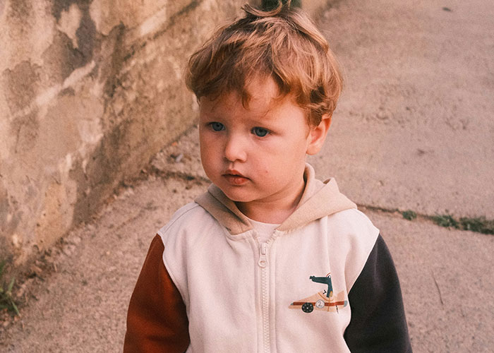Toddler boy with curly hair wearing a color-block jacket outdoors, illustrating kids embarrassing moms moments.
