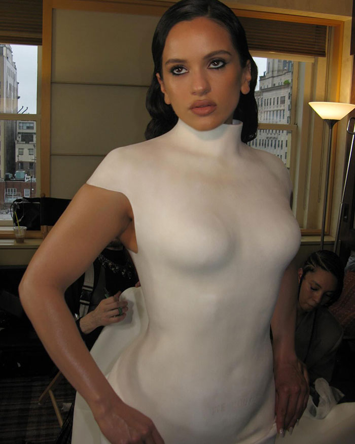 Pop star at Paris Fashion Week wearing a white body suit with bold makeup and styled hair posing indoors.