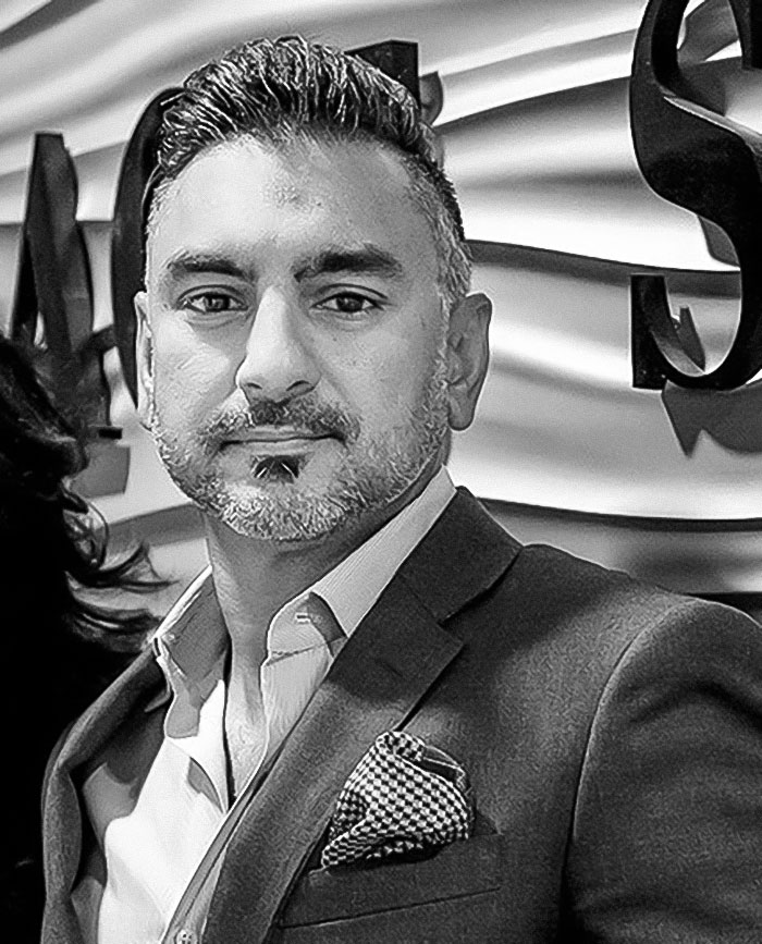 Male dentist in a suit, posing confidently indoors with textured wall background, related to morbidly obese patient tooth removal.