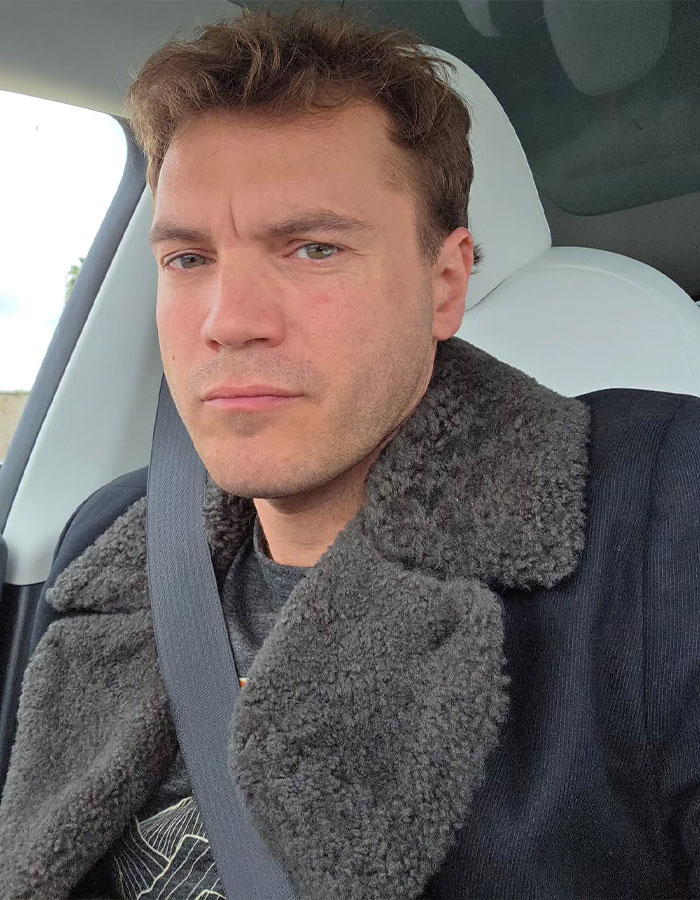 Close-up of a famous man wearing a dark shearling coat and seatbelt inside a car, illustrating famous men shorter than fans imagined.