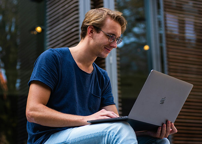 Young man using laptop outdoors, discovering useful life hacks accidentally while working in a casual setting