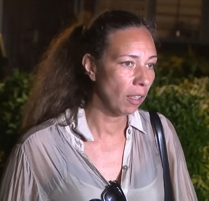 Woman with long hair tied back wearing a light shirt discussing the 12YO subway surfing accident and parental blame outdoors at night.