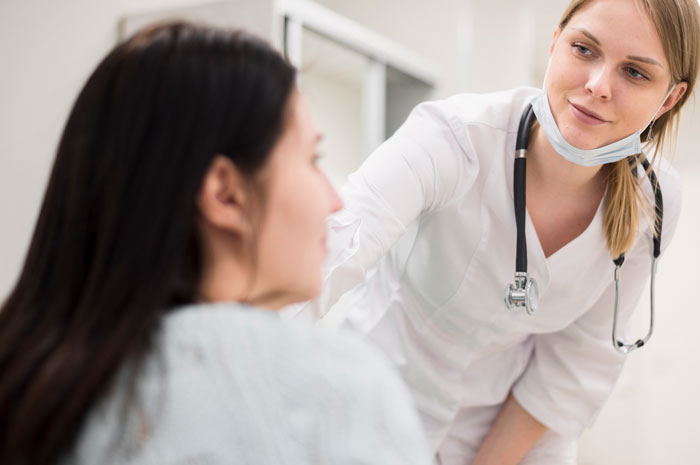 Daycare worker wearing scrubs and stethoscope attentively listening to a parent's family secrets in a clinical setting.