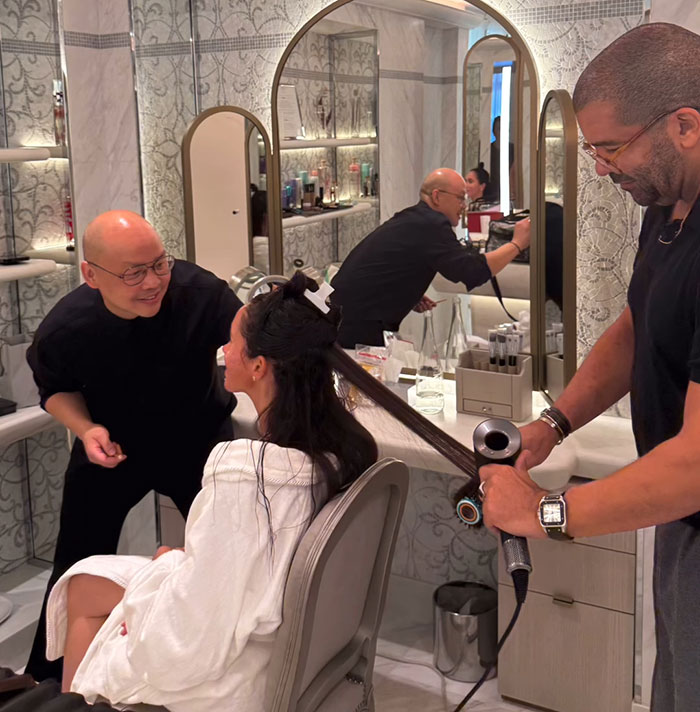Hairstylists preparing a woman&rsquo;s hair in a salon, related to Meghan Markle Paris Fashion Week Balenciaga designer story.