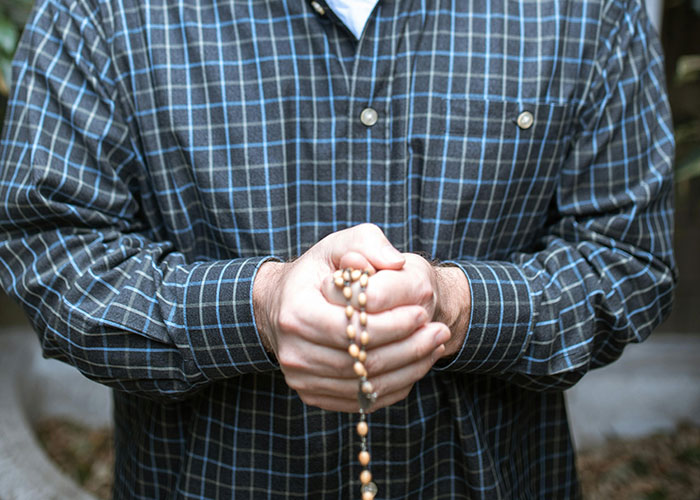 Person wearing a checkered shirt holding a wooden bead necklace, illustrating clever loopholes used against horrible bosses.