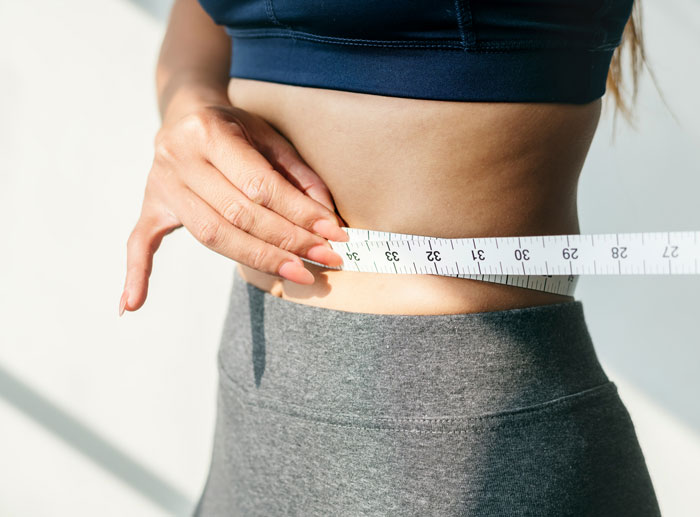 Close-up of a person measuring their waist, illustrating plastic surgeons and unnecessary surgeries related to body contouring.