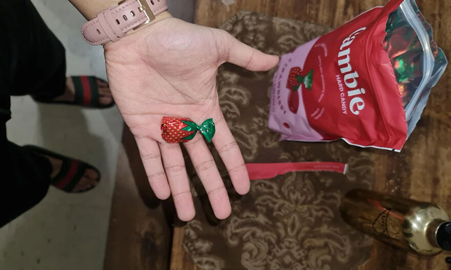 Hand holding strawberry-shaped candy next to an open bag of candy, illustrating popular Halloween candy rankings.
