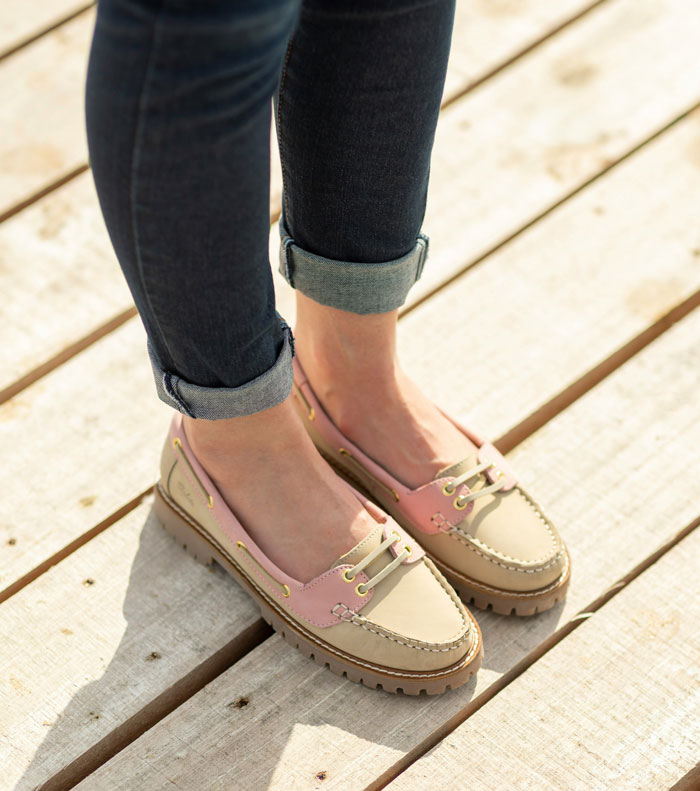 Person wearing beige and pink shoes with rolled-up dark jeans on wooden flooring, representing worst employees concept.