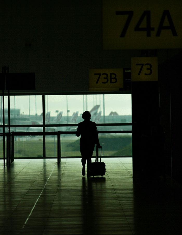 Silhouette of a traveler with luggage in an airport terminal near gate signs, related to NYPD detective and cosmetic surgery case.